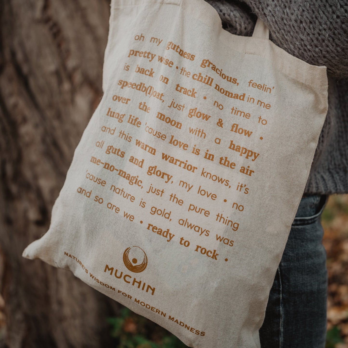 Person holding a tote bag with text and a visible brand logo from Muchin.