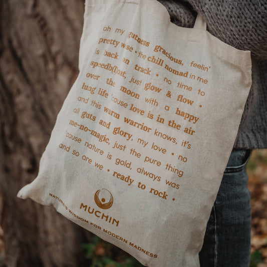 Person holding a tote bag with text and a visible brand logo from Muchin.